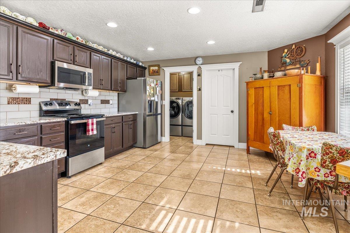 Kitchen featuring appliances with stainless steel finishes, dark brown cabinetry, a textured ceiling, backsplash, and washing machine and dryer
