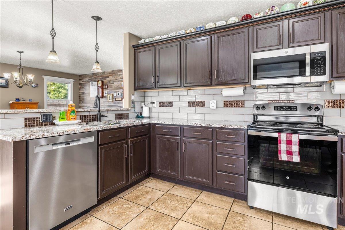 Kitchen with stainless steel appliances, dark brown cabinets, a peninsula, a textured ceiling, and light stone countertops