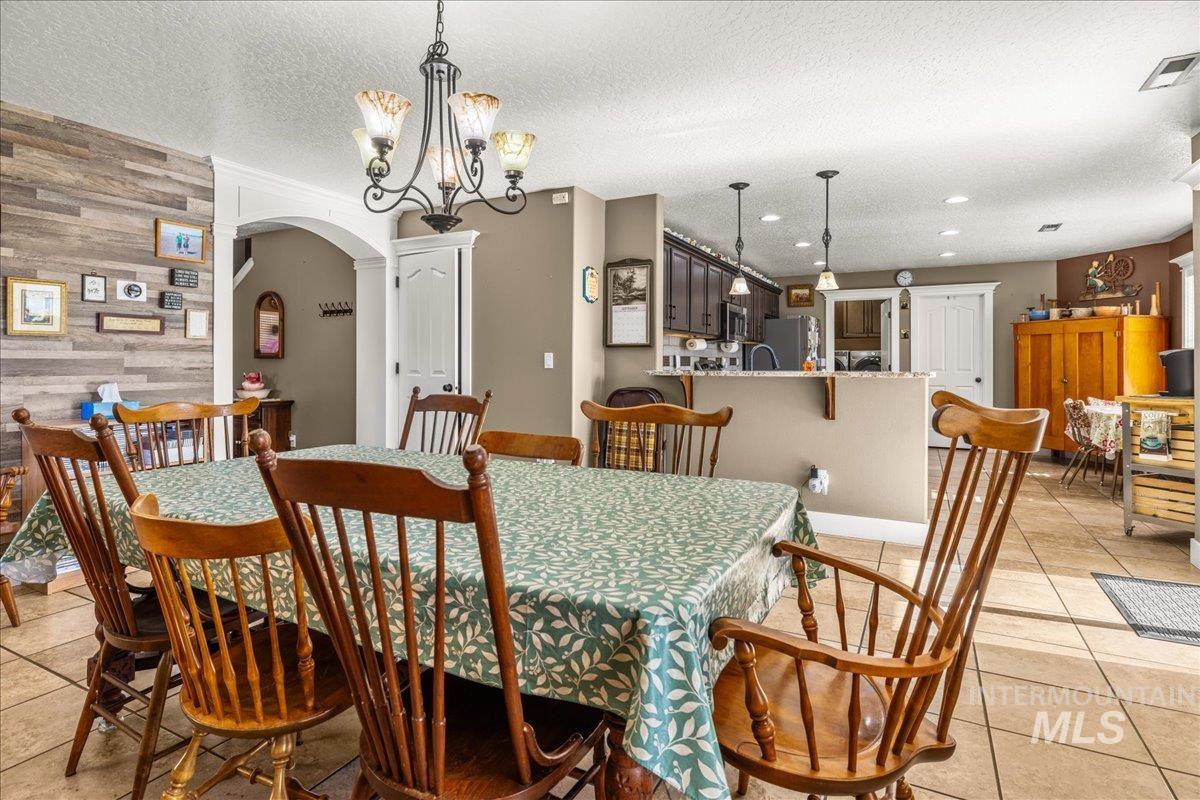 Dining room featuring light tile patterned flooring, wooden walls, arched walkways, a chandelier, and an accent wall