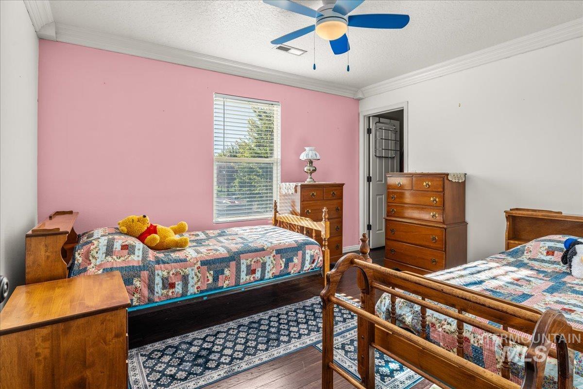 Bedroom featuring crown molding, dark wood-style flooring, a textured ceiling, and ceiling fan
