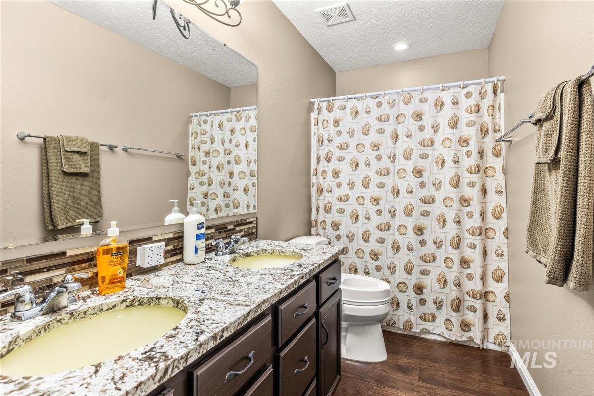 Bathroom featuring dark wood-type flooring, a textured ceiling, double vanity, and a shower with curtain