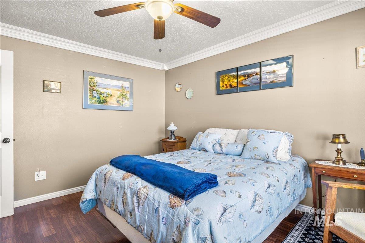 Bedroom featuring a textured ceiling, crown molding, wood finished floors, and a ceiling fan