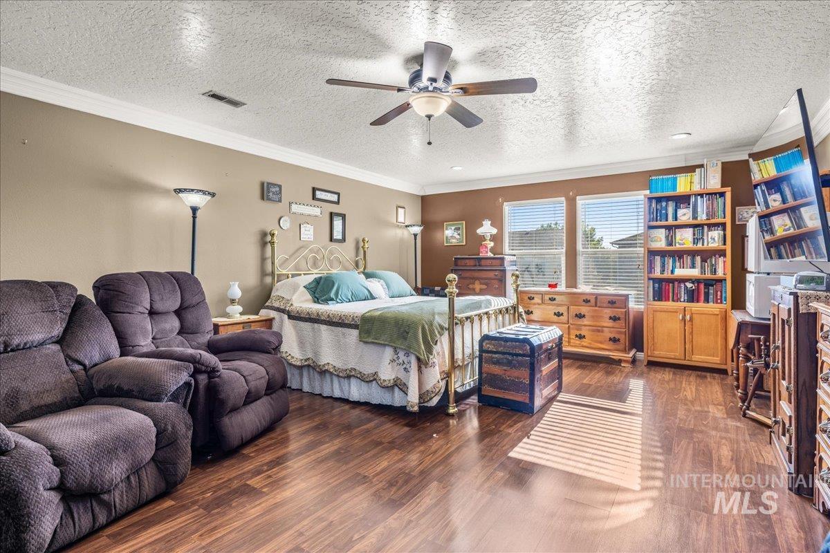 Bedroom featuring a textured ceiling, crown molding, dark wood finished floors, and a ceiling fan