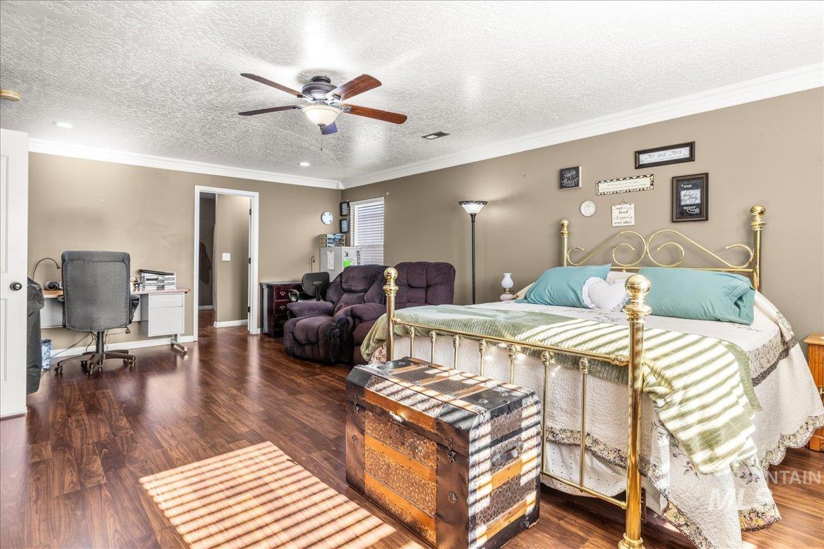 Bedroom with ornamental molding, a textured ceiling, dark wood-style floors, an office area, and ceiling fan
