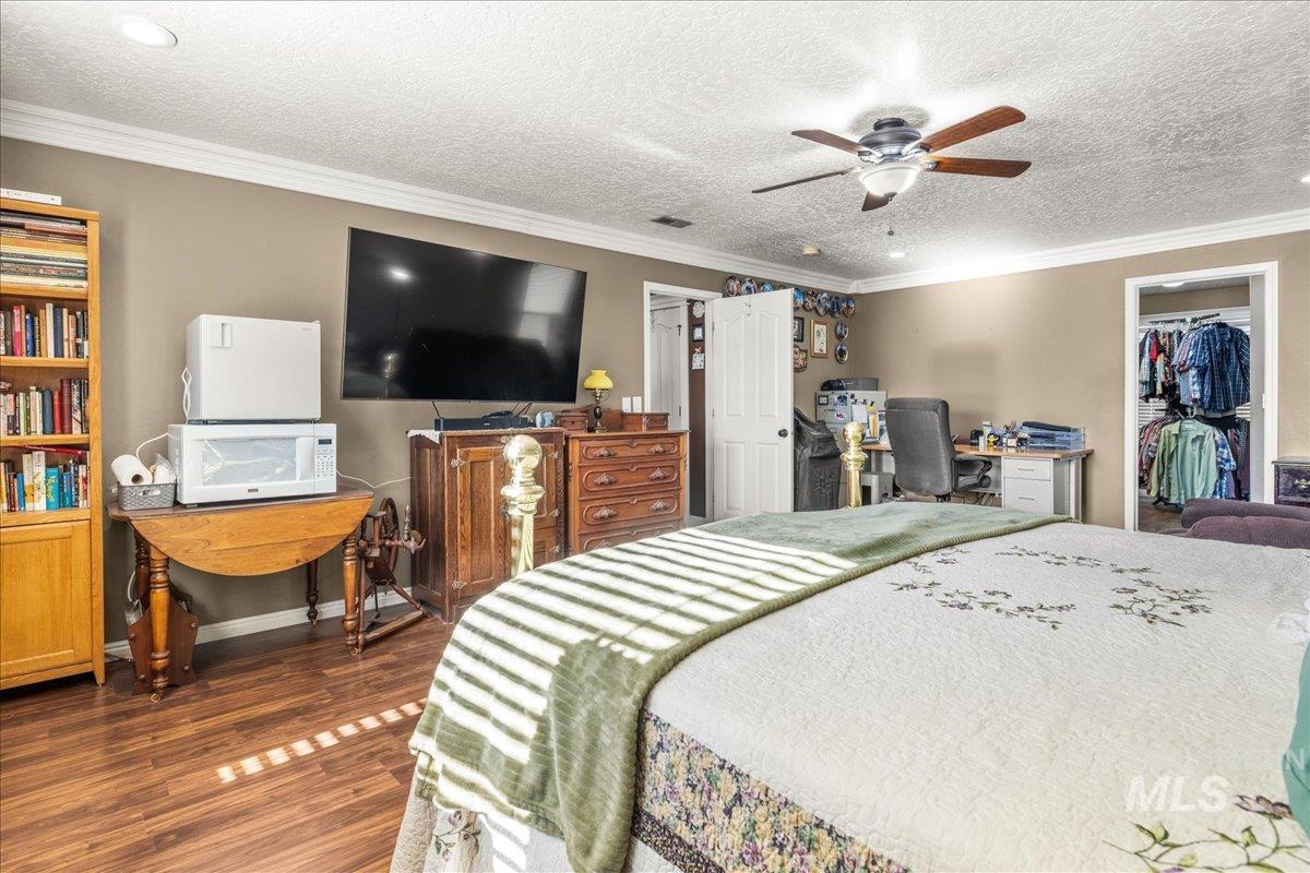 Bedroom featuring crown molding, dark wood-style floors, a textured ceiling, a walk in closet, and a ceiling fan