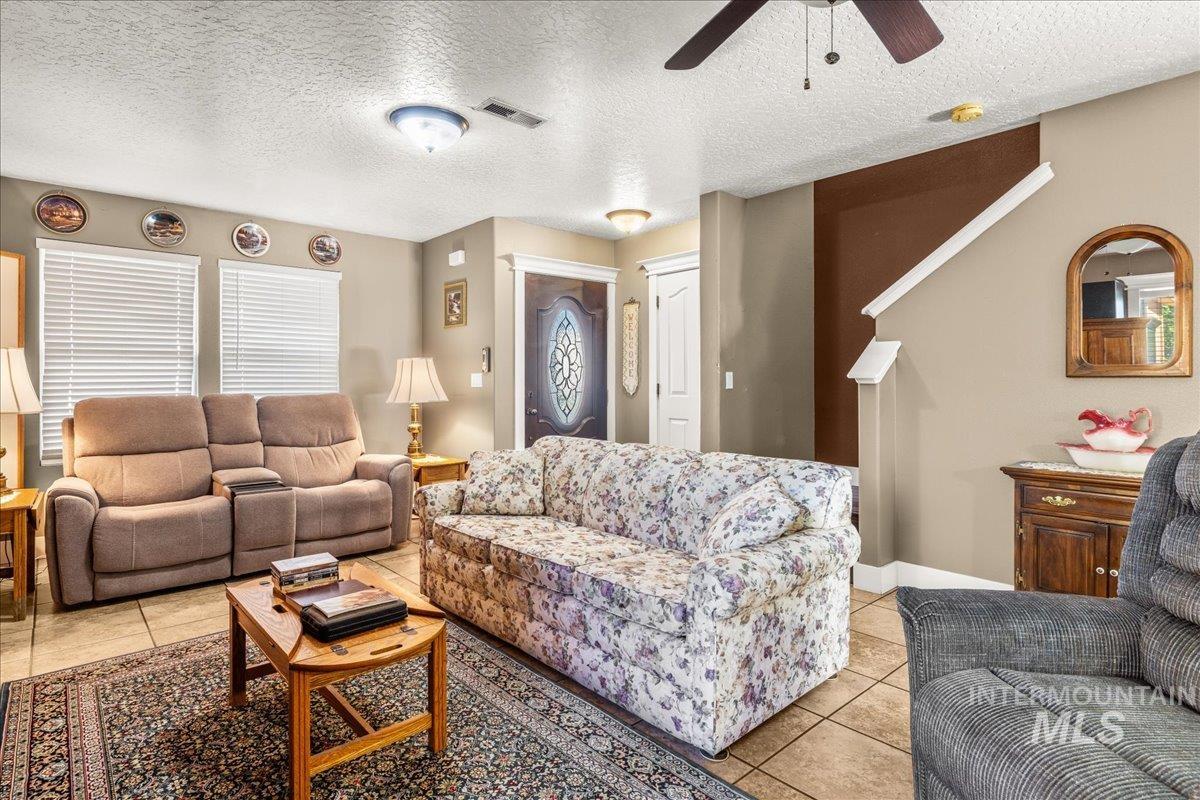 Living area with a textured ceiling, light tile patterned floors, and a ceiling fan