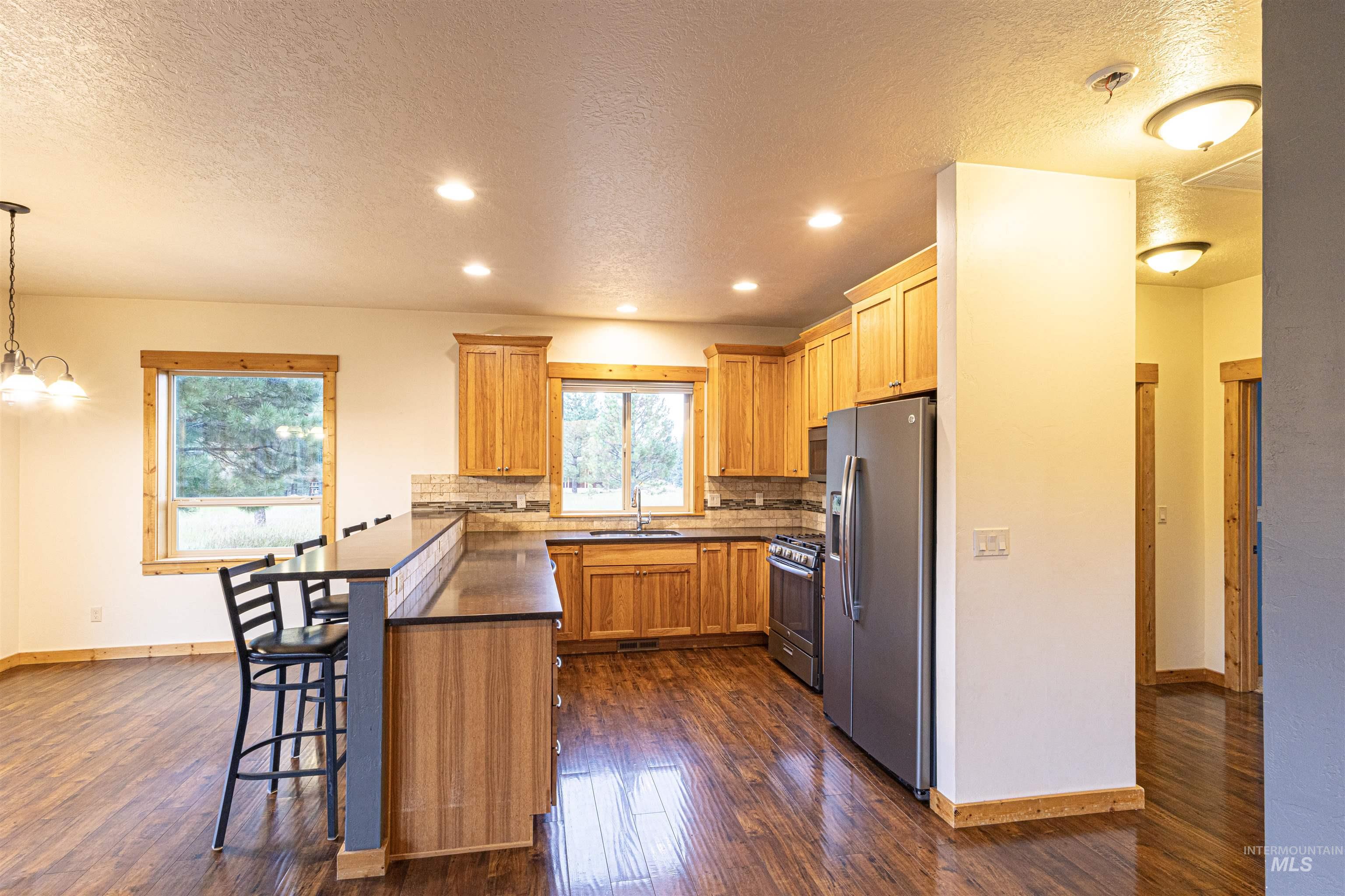 Kitchen featuring a peninsula, a textured ceiling, a kitchen breakfast bar, stainless steel appliances, and dark countertops