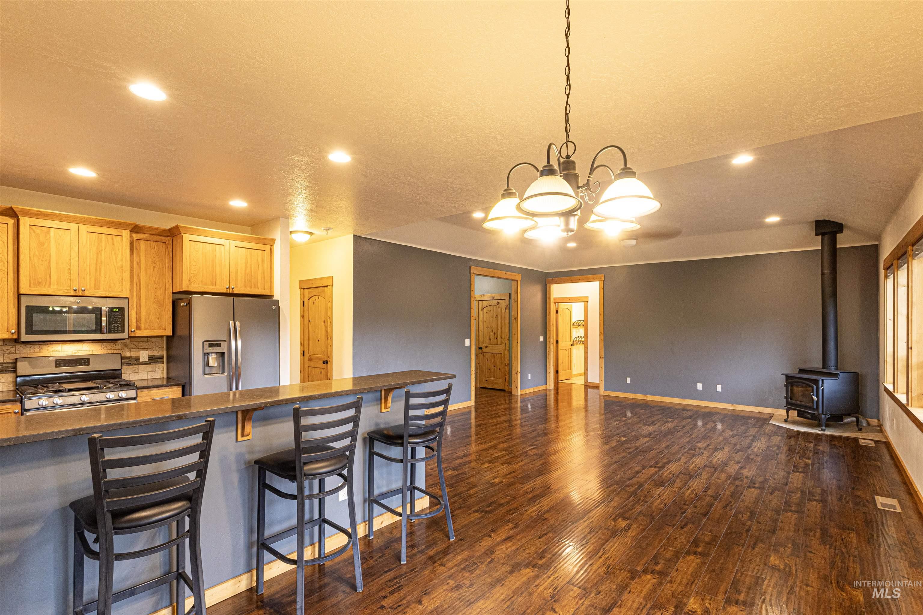 Kitchen featuring a wood stove, a breakfast bar, appliances with stainless steel finishes, hanging light fixtures, and dark stone countertops