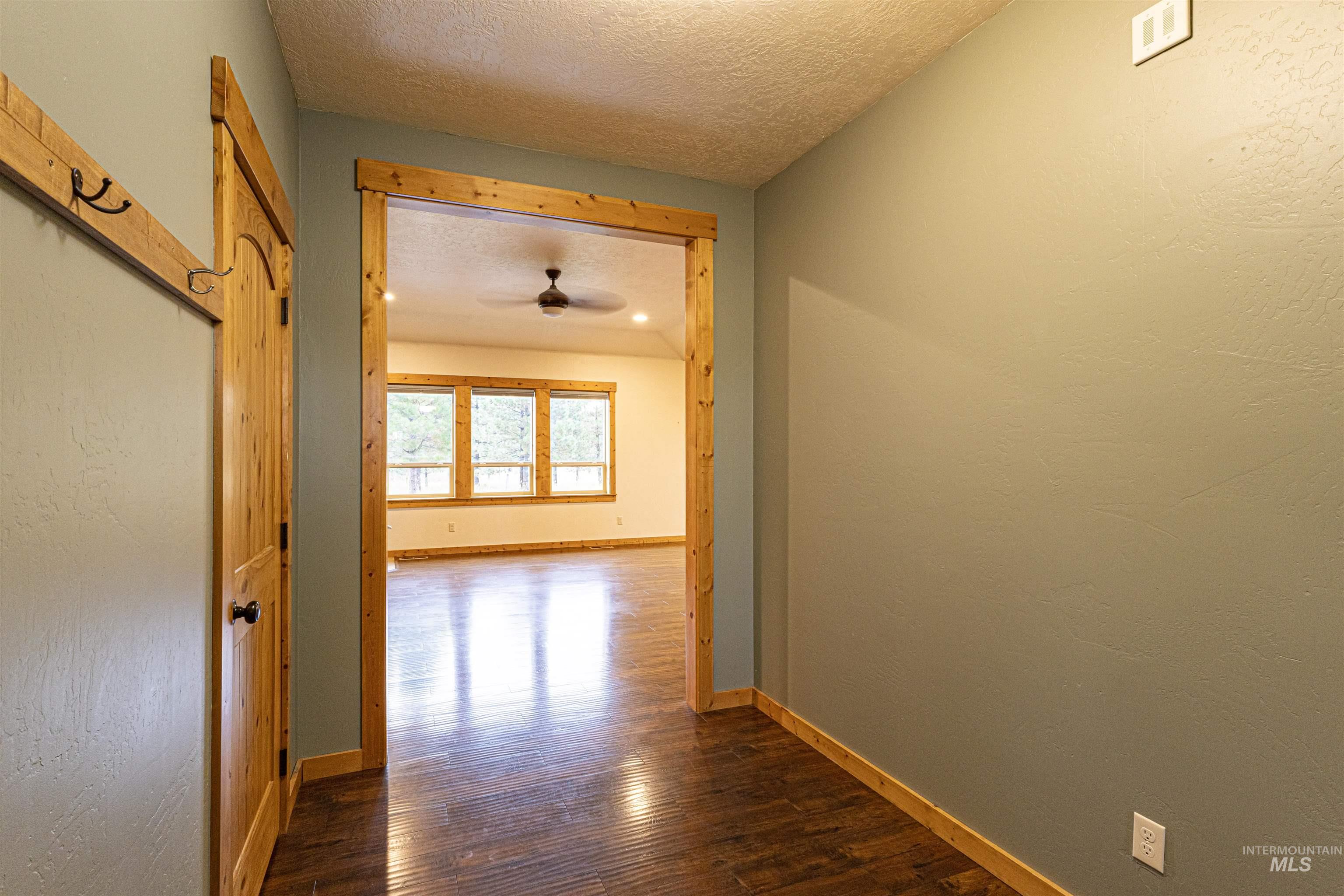 Hallway featuring a textured ceiling, dark wood-style flooring, and a textured wall