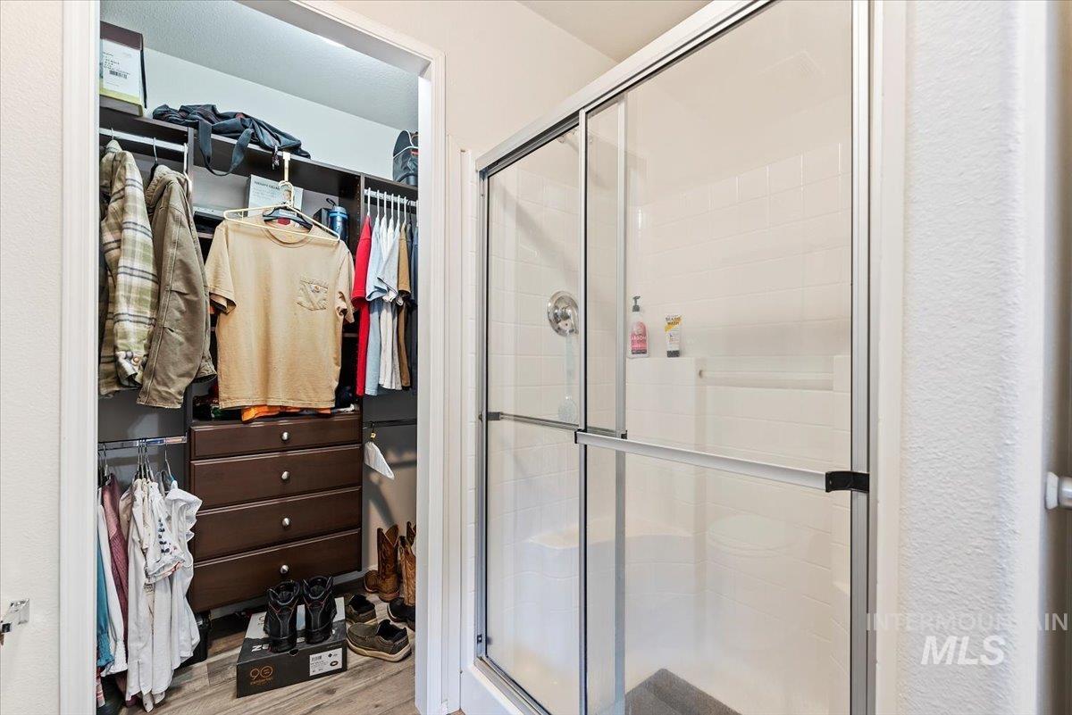 Full bath with a spacious closet, a stall shower, and light wood finished floors