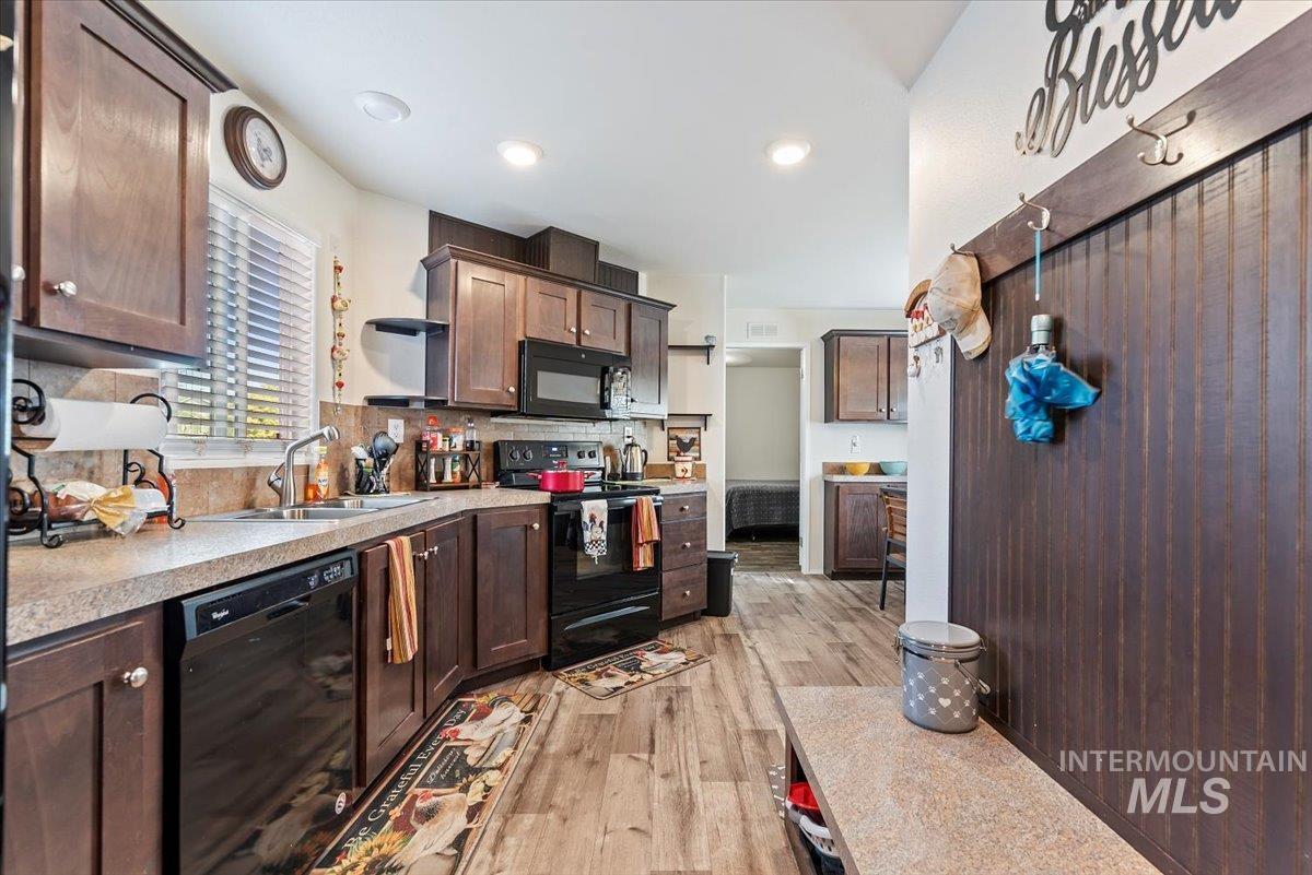 Kitchen featuring black appliances, light countertops, light wood-type flooring, dark brown cabinetry, and backsplash