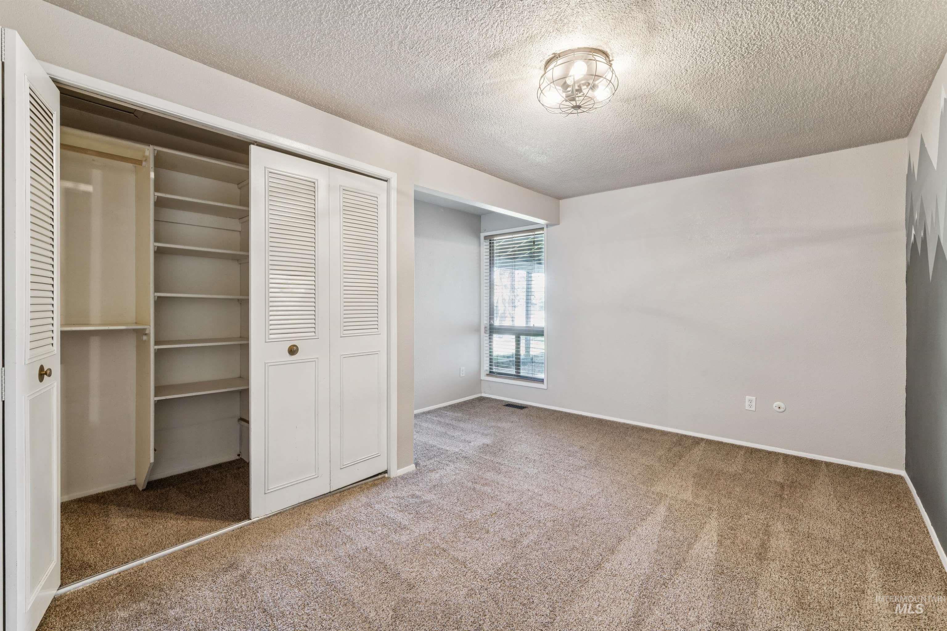 Unfurnished bedroom with a closet, light colored carpet, and a textured ceiling