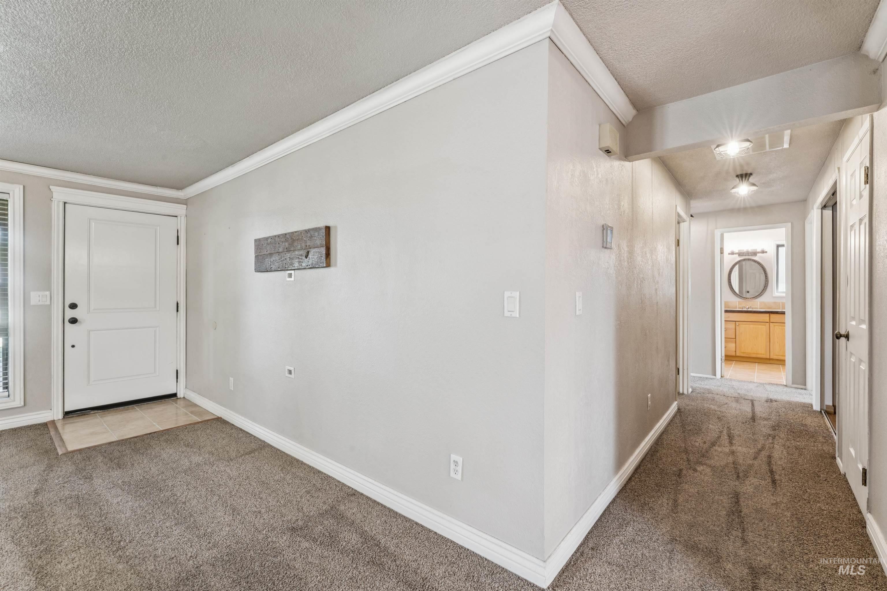 Tiled foyer entrance with carpet floors, a textured ceiling, and crown molding