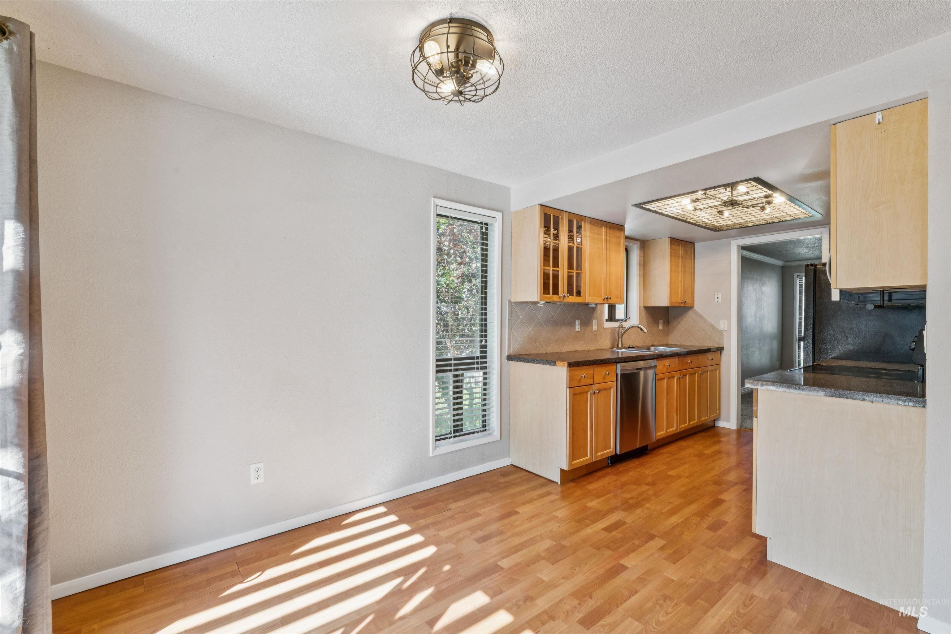 Kitchen with tasteful backsplash, glass insert cabinets, light wood-style flooring, stainless steel dishwasher, and dark stone countertops