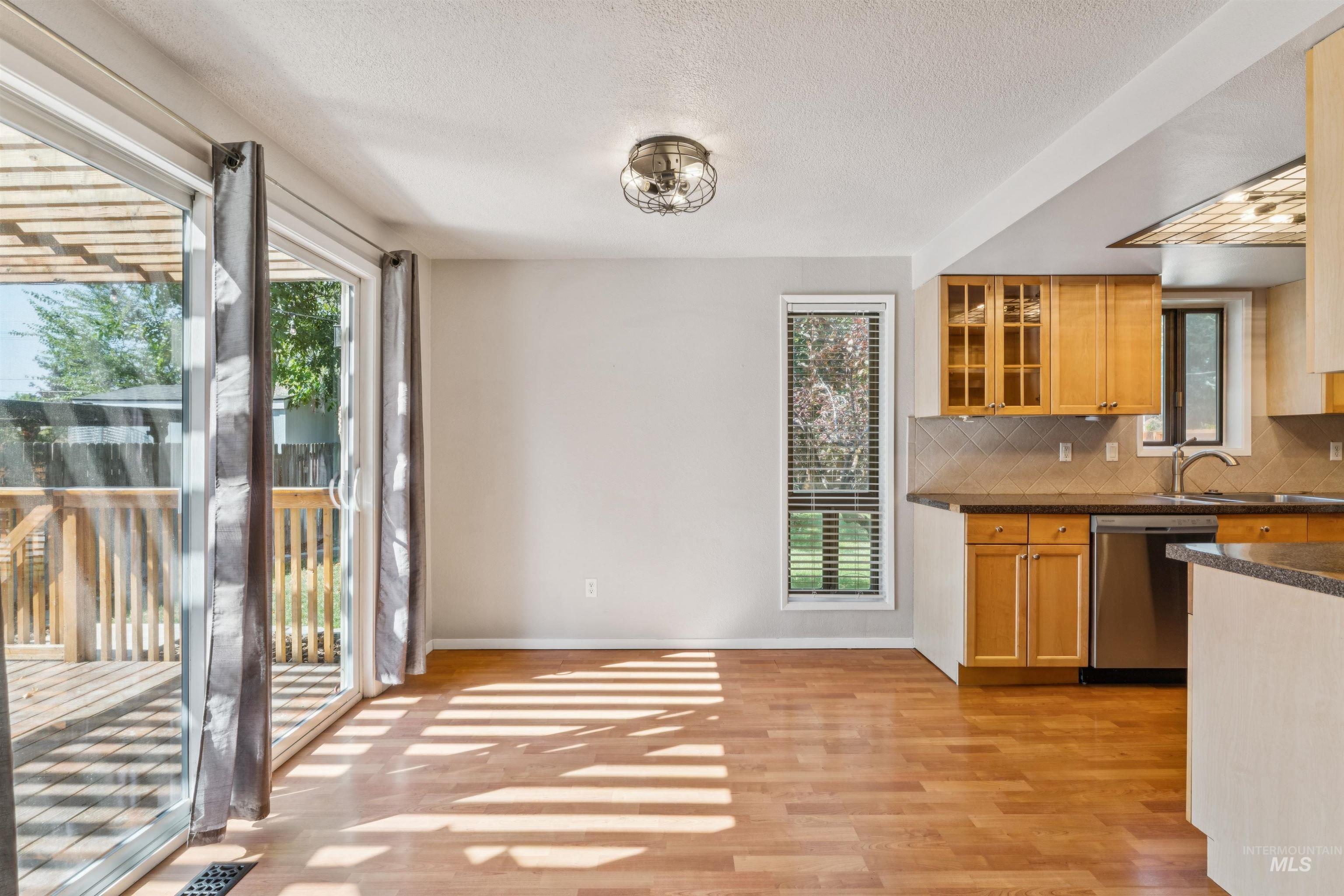 Kitchen featuring decorative backsplash, glass insert cabinets, dishwasher, light wood-style floors, and dark stone countertops