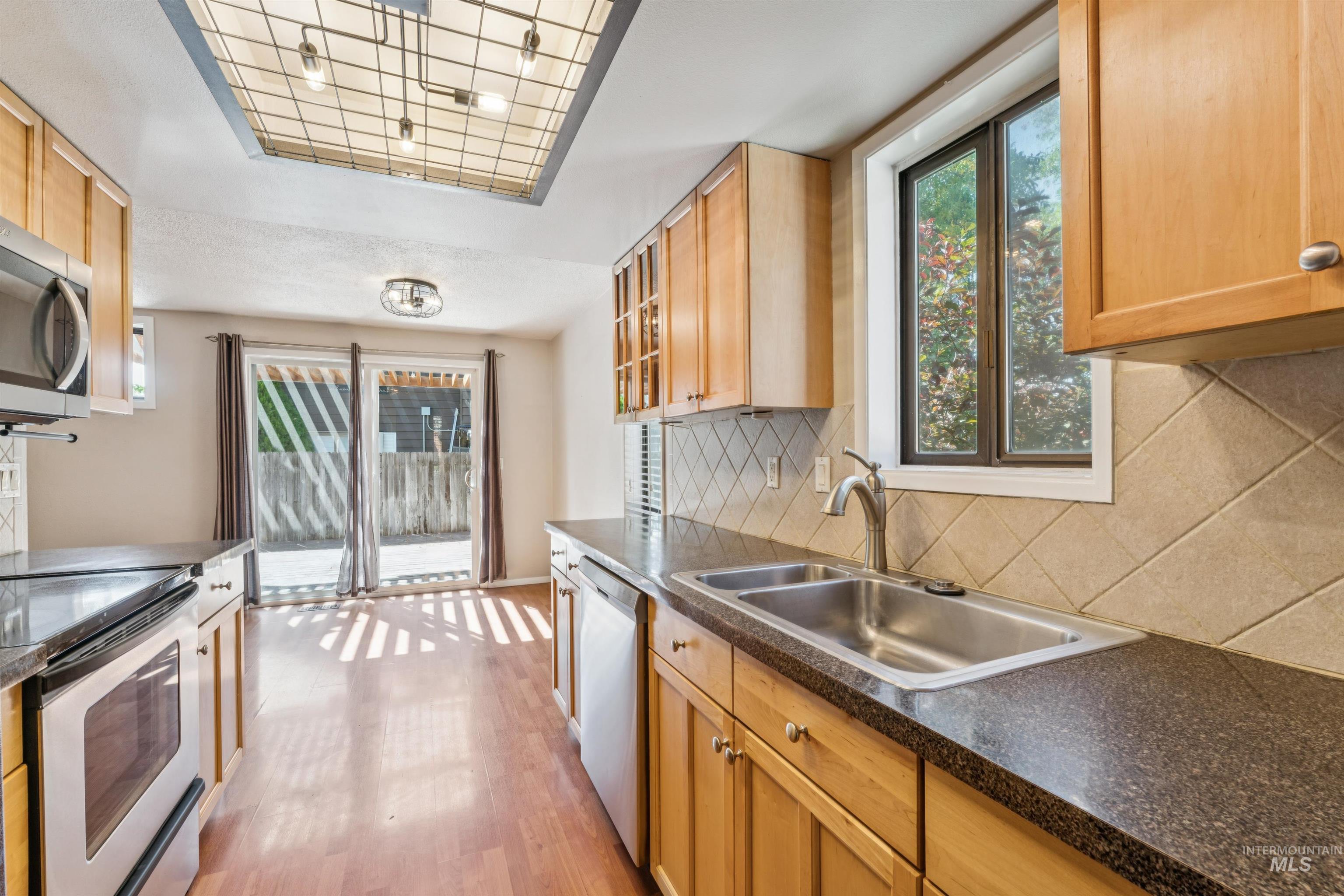 Kitchen featuring stainless steel appliances, healthy amount of natural light, light wood finished floors, and dark countertops