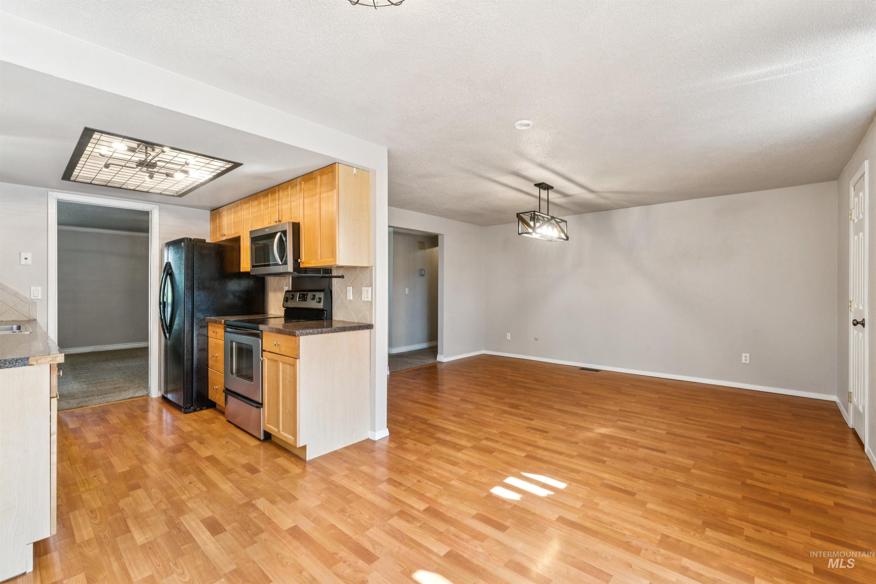 Kitchen featuring appliances with stainless steel finishes, pendant lighting, light wood-type flooring, backsplash, and open floor plan