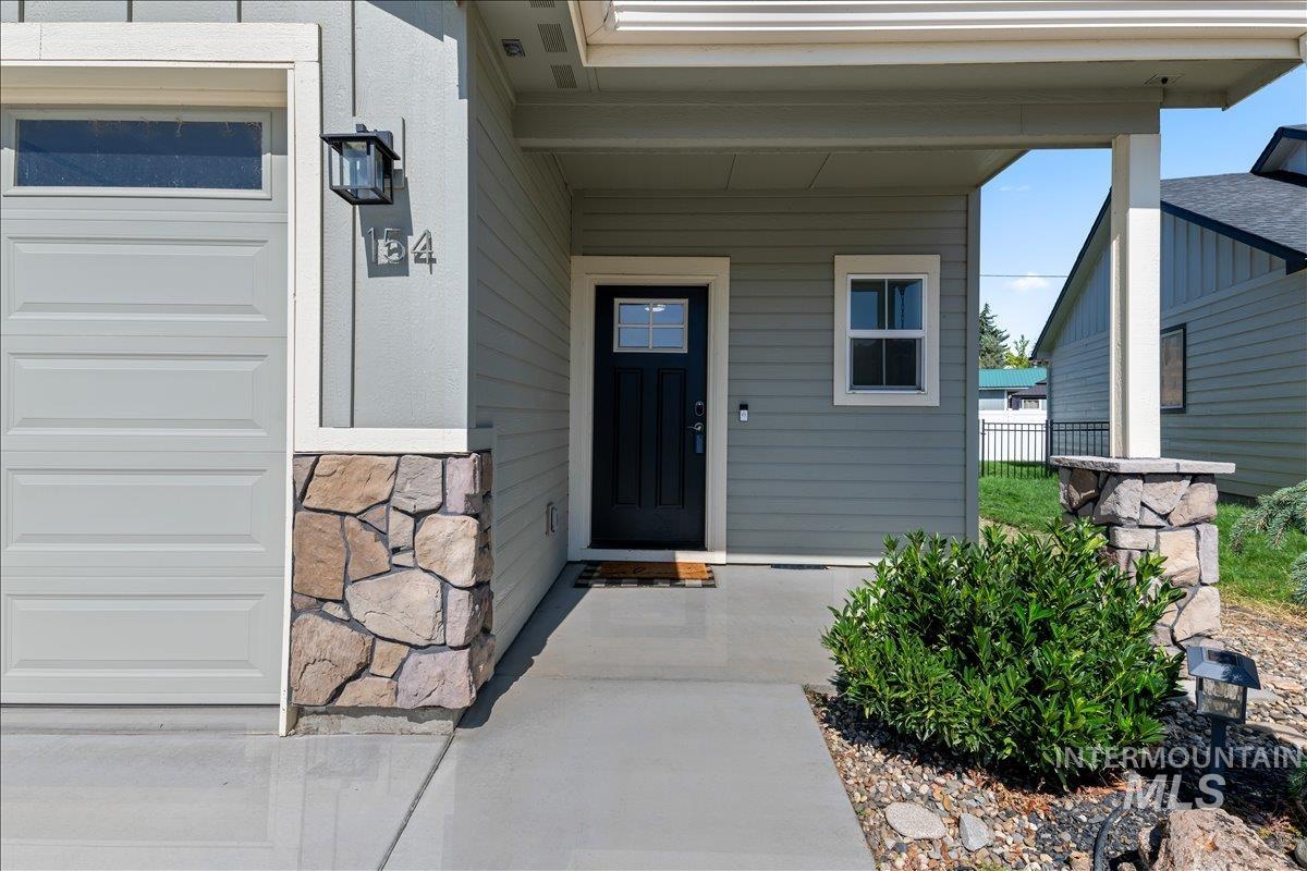 Entrance to property with covered porch, stone siding, and a garage