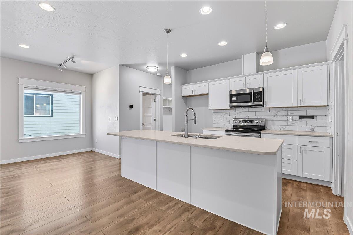 Kitchen with backsplash, white cabinets, pendant lighting, appliances with stainless steel finishes, and a kitchen island with sink