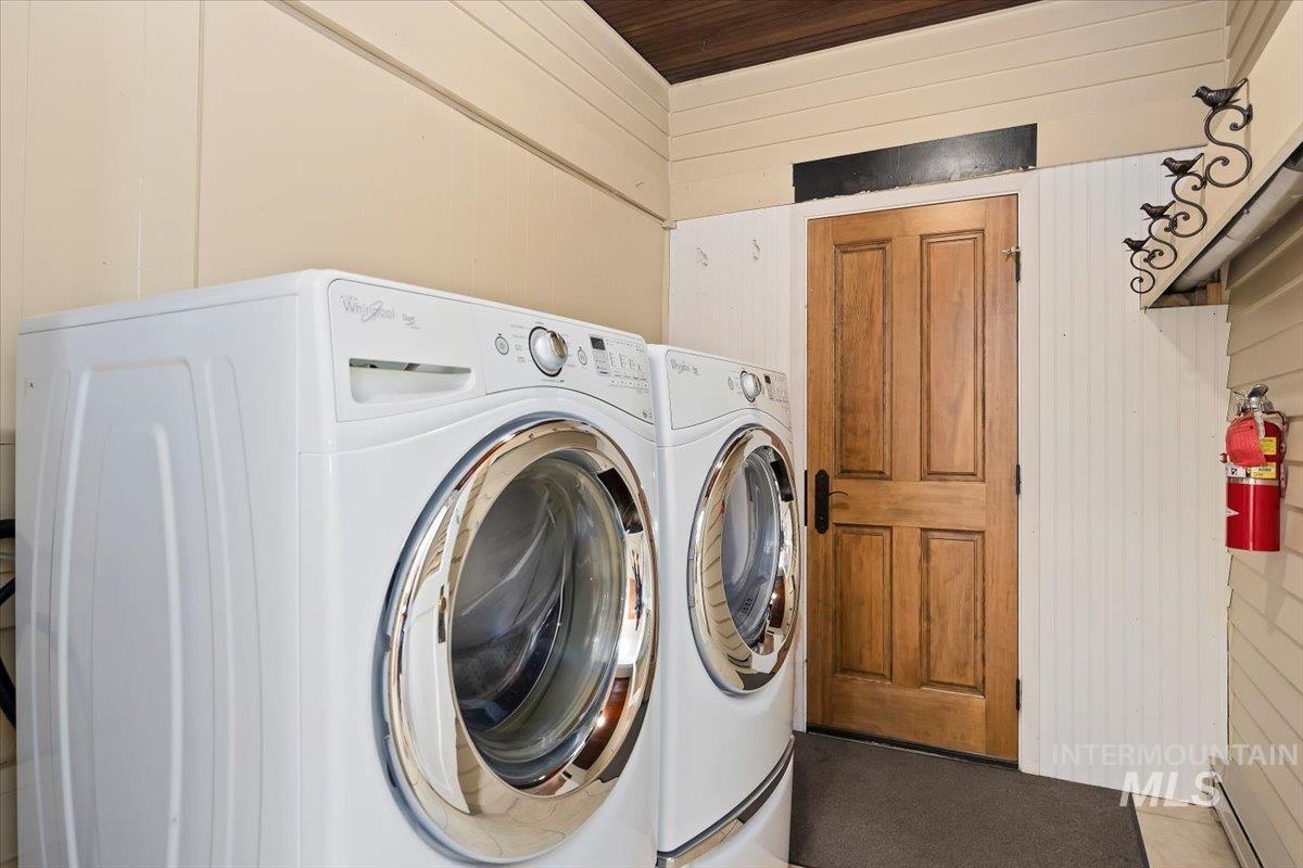 Washroom featuring wooden walls, washing machine and dryer, and a baseboard heating unit