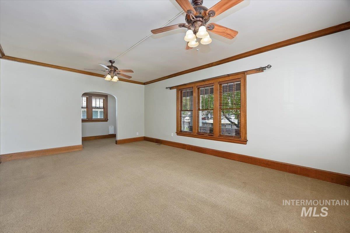 Empty room featuring ornamental molding, light colored carpet, arched walkways, and ceiling fan