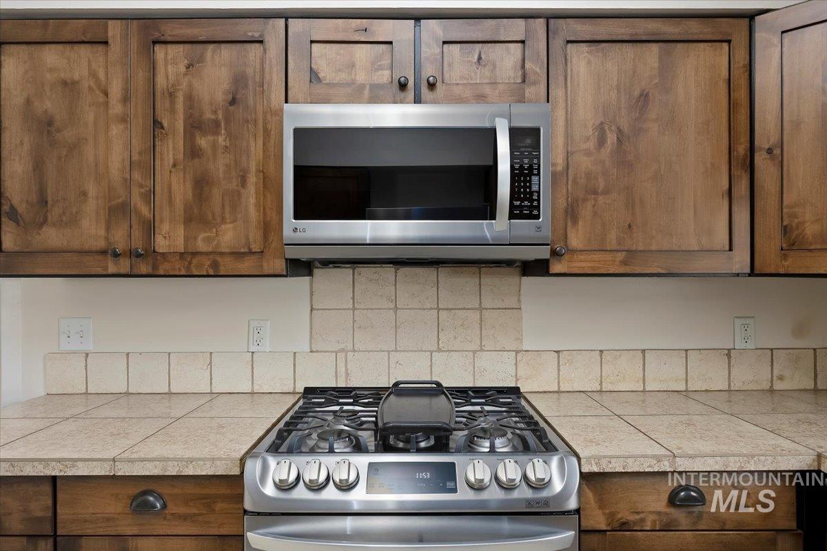 Kitchen with stainless steel appliances, tile countertops, and brown cabinetry