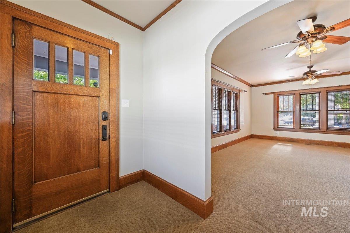 Foyer featuring crown molding, plenty of natural light, a ceiling fan, and carpet flooring