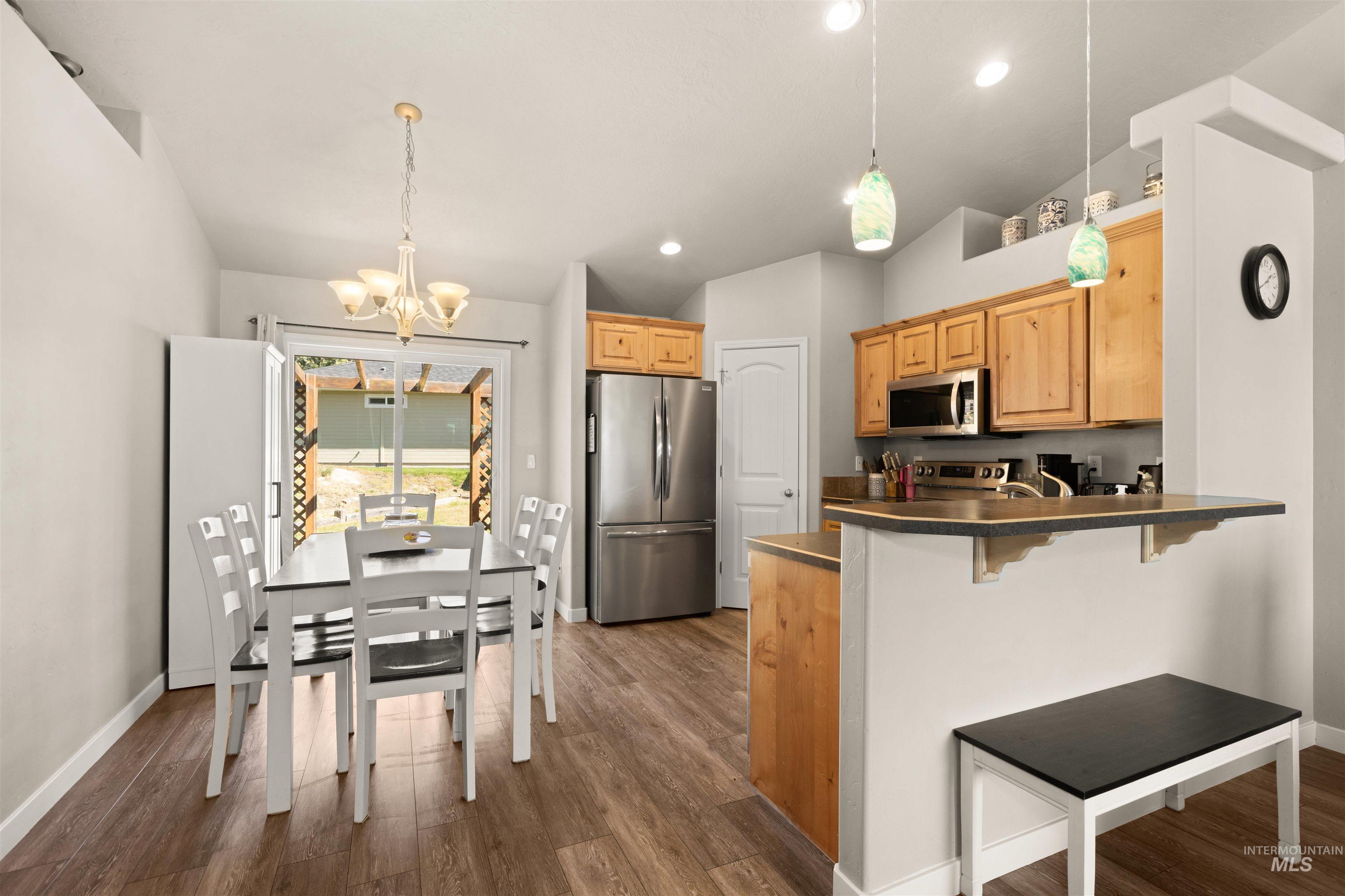 Kitchen featuring dark countertops, pendant lighting, vaulted ceiling, stainless steel appliances, and a kitchen breakfast bar