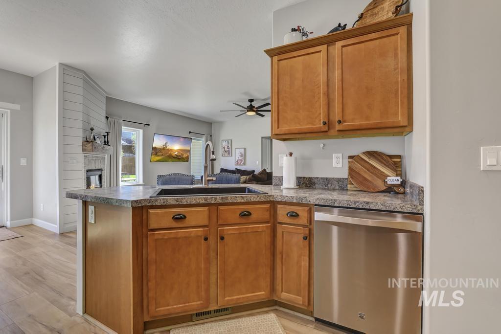 Kitchen with a peninsula, brown cabinetry, open floor plan, dishwasher, and a ceiling fan