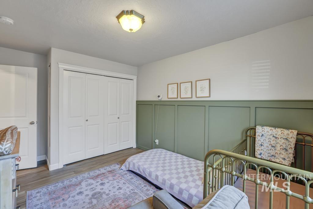 Bedroom featuring a decorative wall, wood finished floors, a closet, and wainscoting
