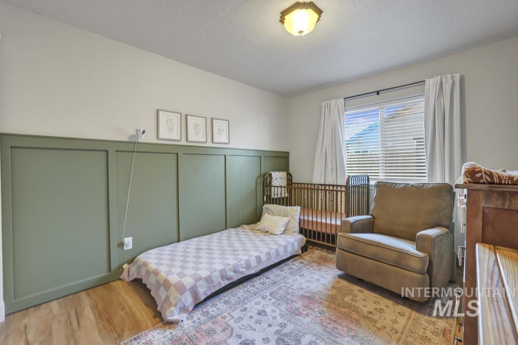 Bedroom with a decorative wall, wood finished floors, and wainscoting