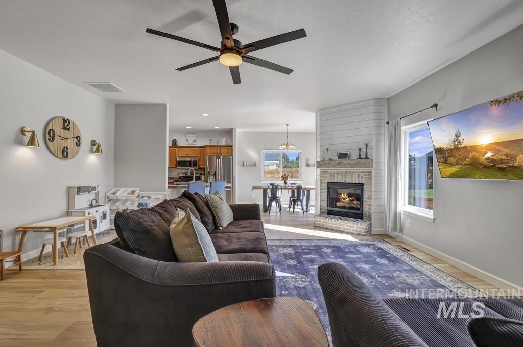 Living area with a ceiling fan, light wood finished floors, and a fireplace