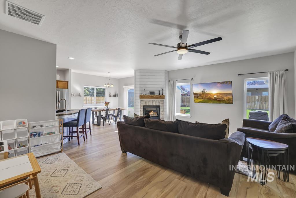 Living area featuring light wood finished floors, a textured ceiling, a fireplace, and a ceiling fan