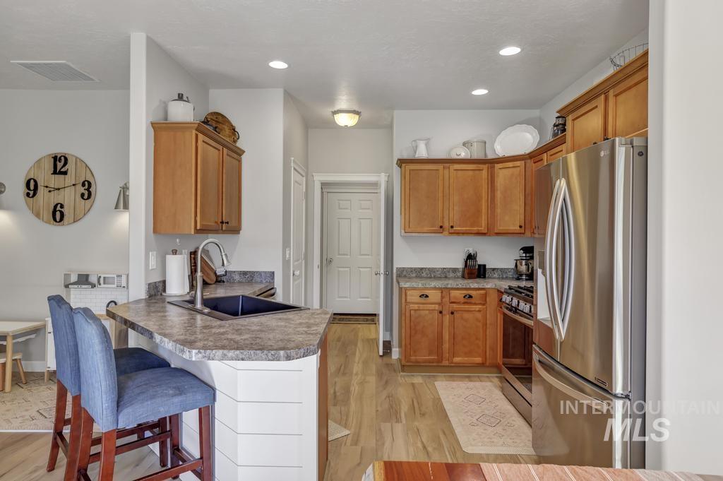 Kitchen featuring stainless steel appliances, a breakfast bar area, light wood-type flooring, brown cabinetry, and a peninsula