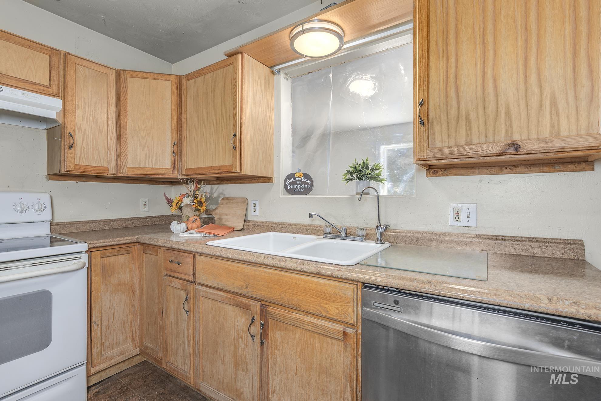 Kitchen with electric range, stainless steel dishwasher, under cabinet range hood, light countertops, and dark tile patterned floors