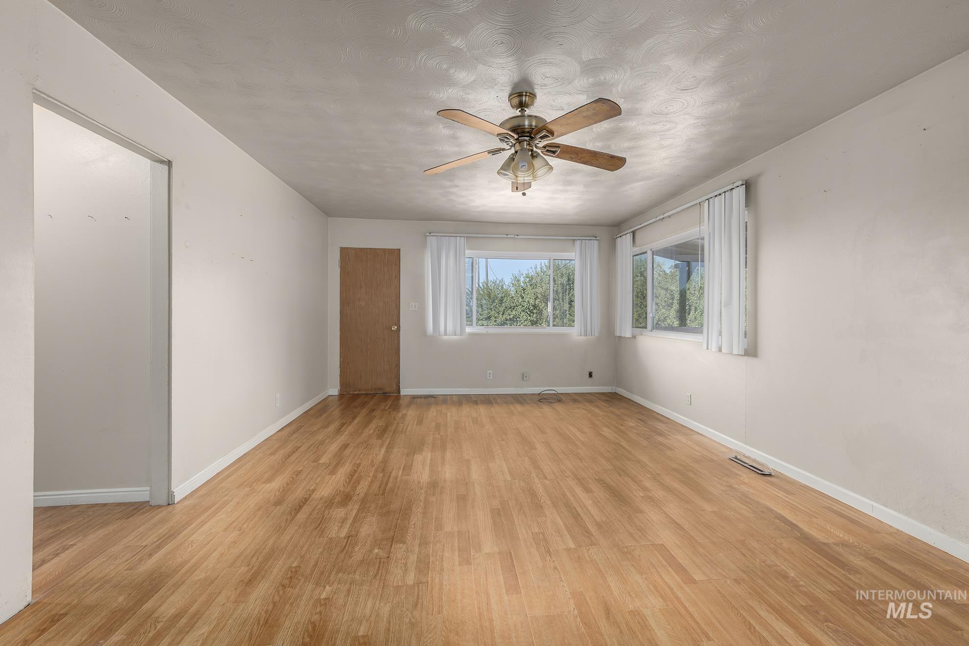 Empty room with light wood-type flooring, a textured ceiling, and a ceiling fan