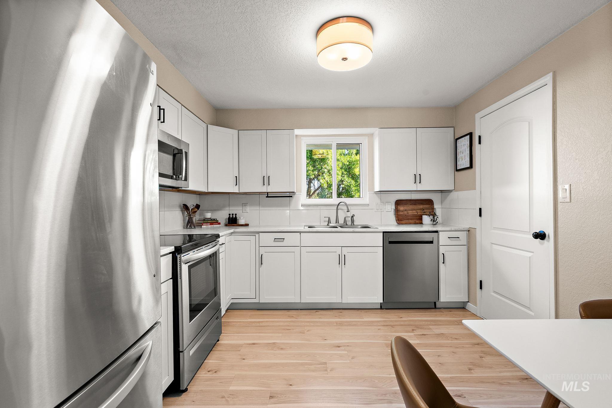 Kitchen with stainless steel appliances, white cabinets, light countertops, light wood-type flooring, and a textured ceiling