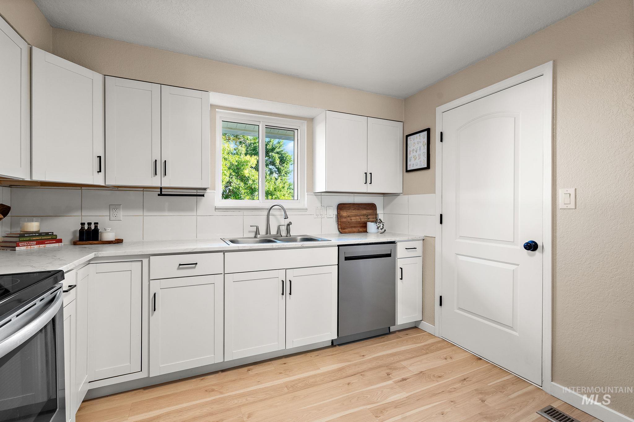 Kitchen with white cabinets, light countertops, light wood finished floors, stainless steel appliances, and backsplash