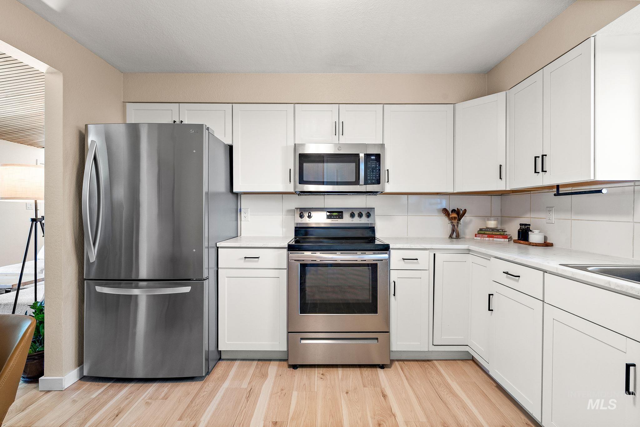 Kitchen featuring stainless steel appliances, white cabinets, and light wood finished floors