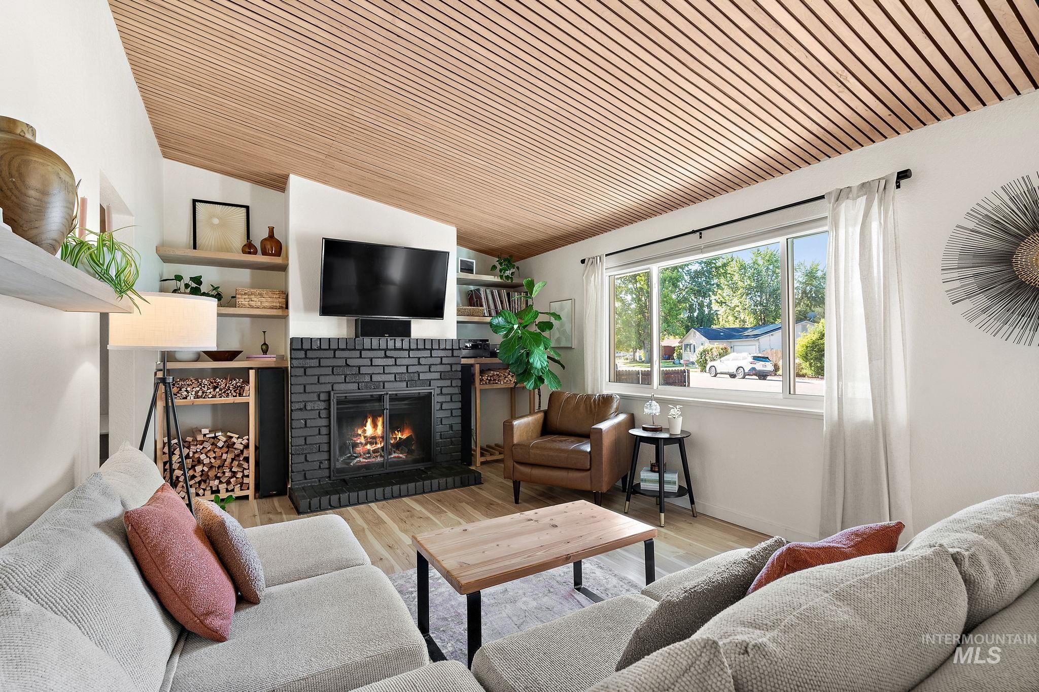 Living room featuring lofted ceiling, wood finished floors, a brick fireplace, and wooden ceiling