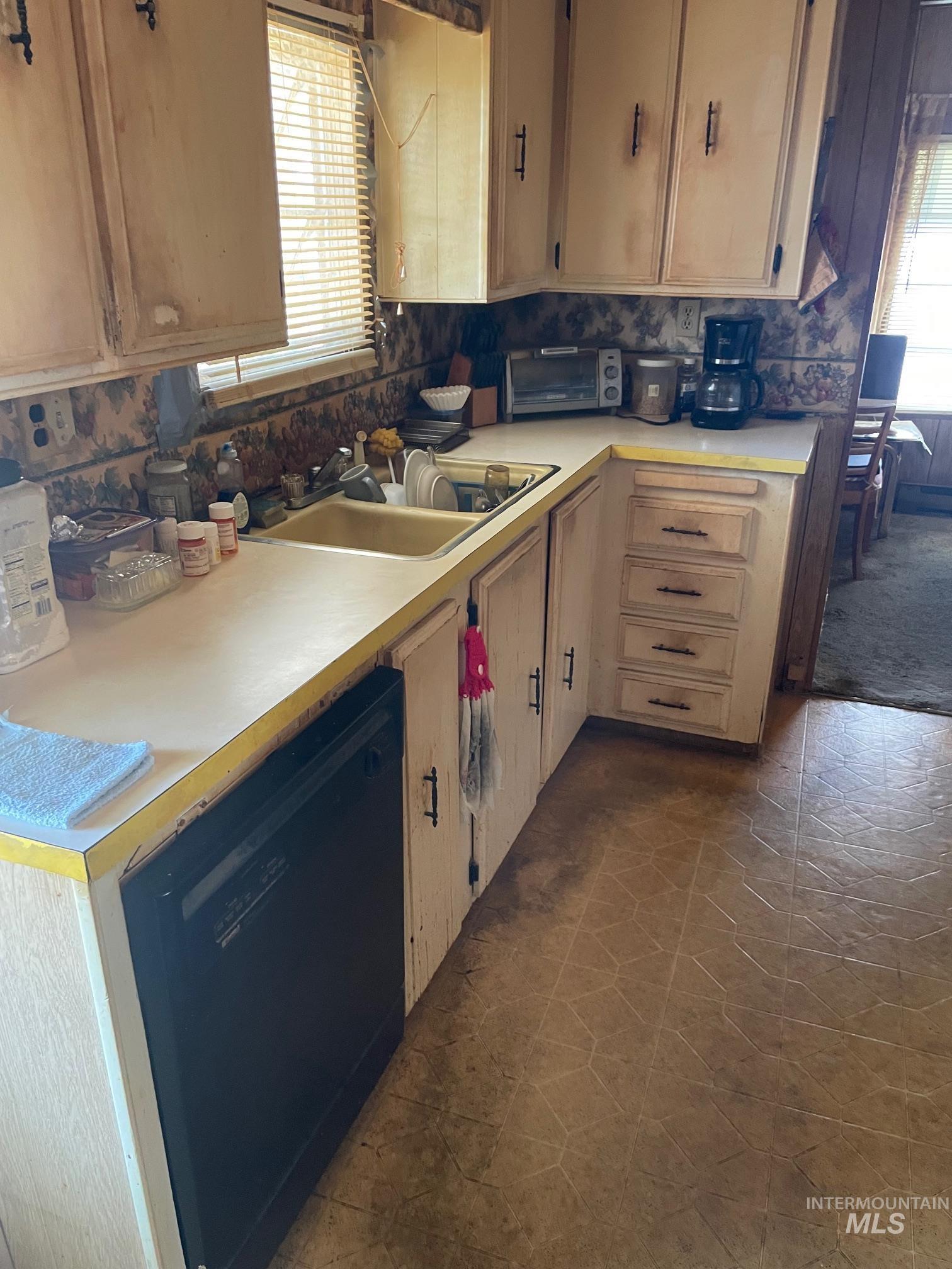Kitchen featuring black dishwasher, light countertops, and light brown cabinetry