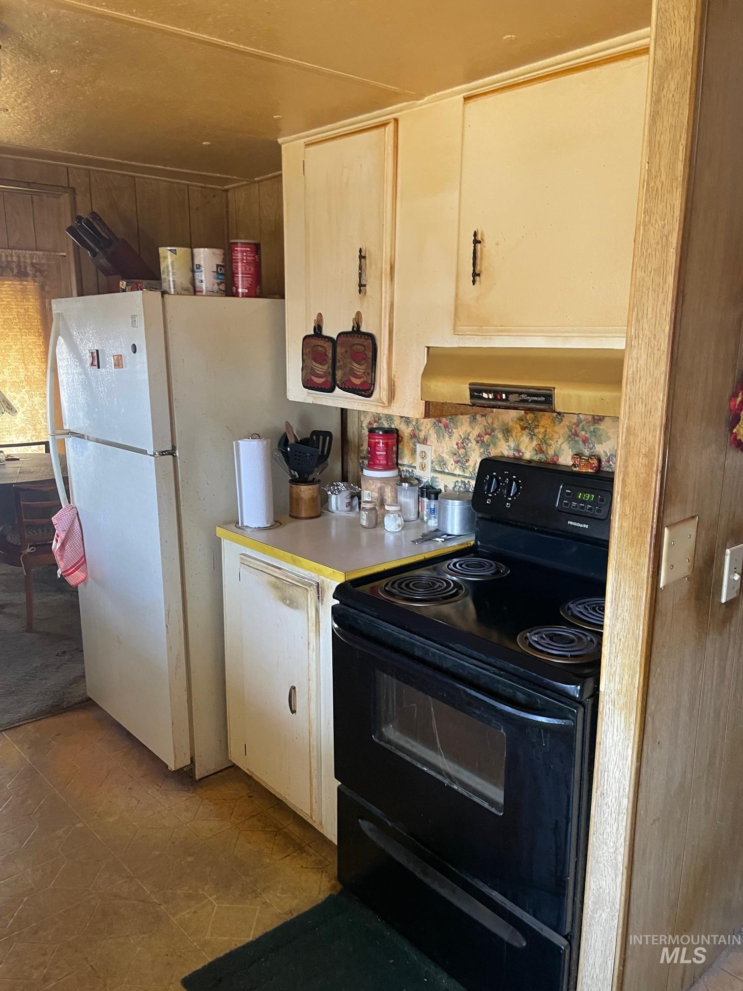 Kitchen with black range with electric stovetop, light countertops, range hood, wood walls, and freestanding refrigerator