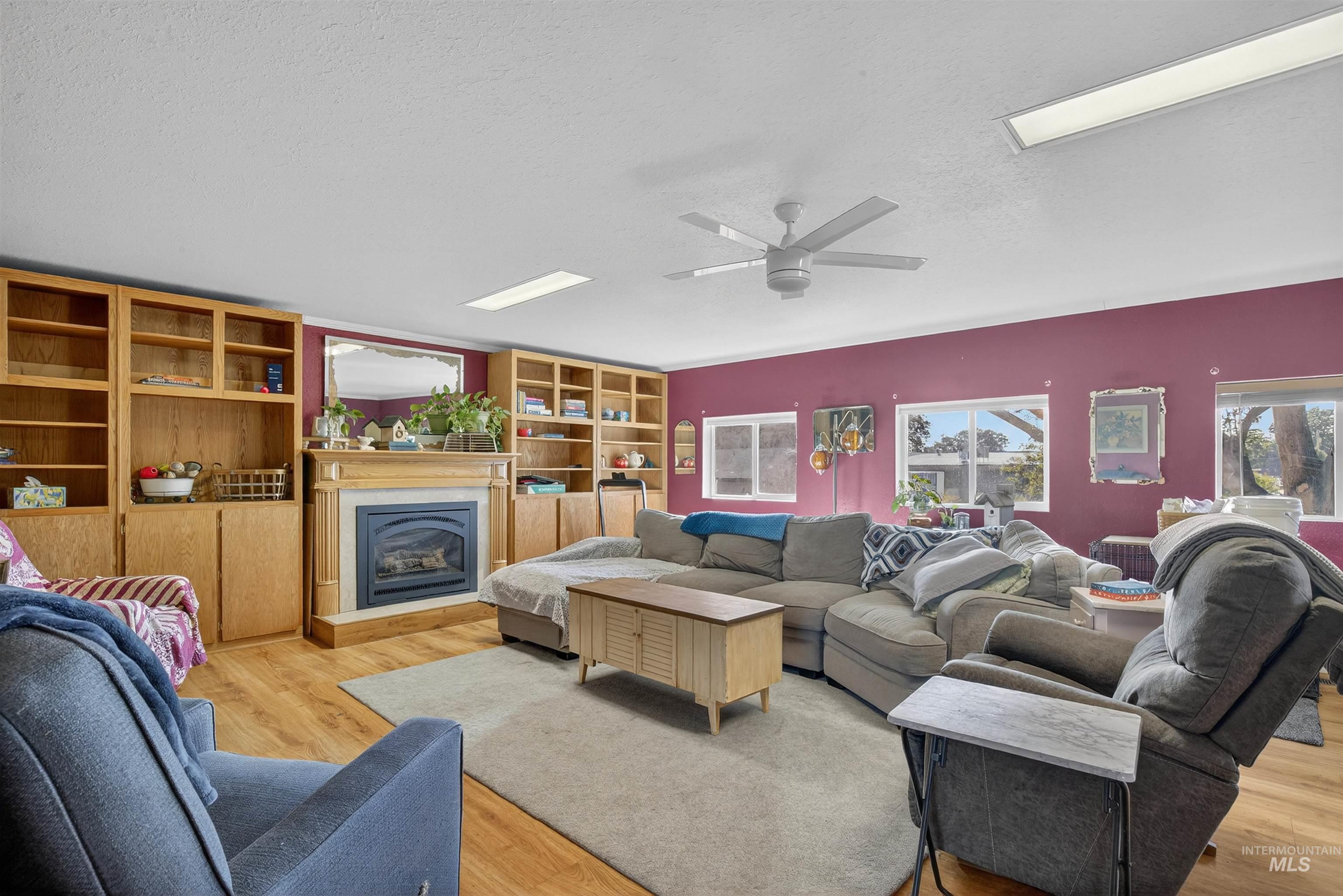 Living area featuring a glass covered fireplace, light wood-style flooring, a textured ceiling, and a ceiling fan
