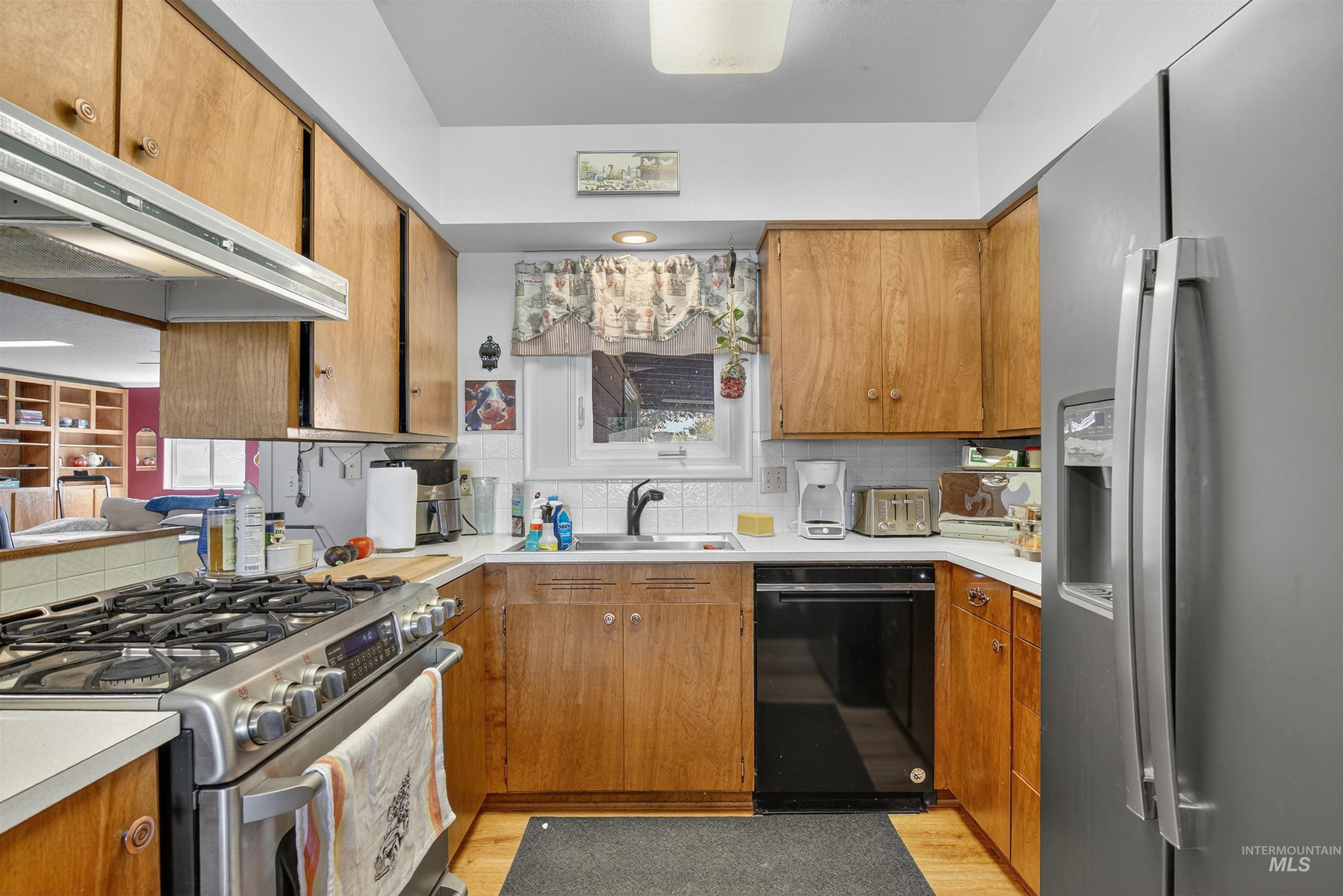Kitchen featuring appliances with stainless steel finishes, light countertops, brown cabinetry, and tasteful backsplash