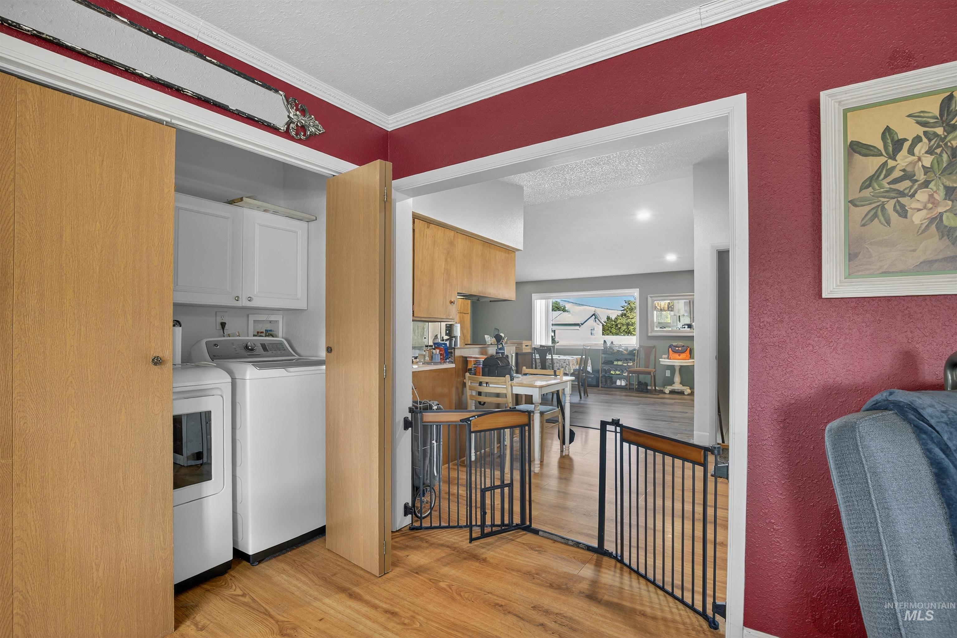 Washroom with light wood-type flooring, cabinet space, washer and dryer, ornamental molding, and a textured ceiling