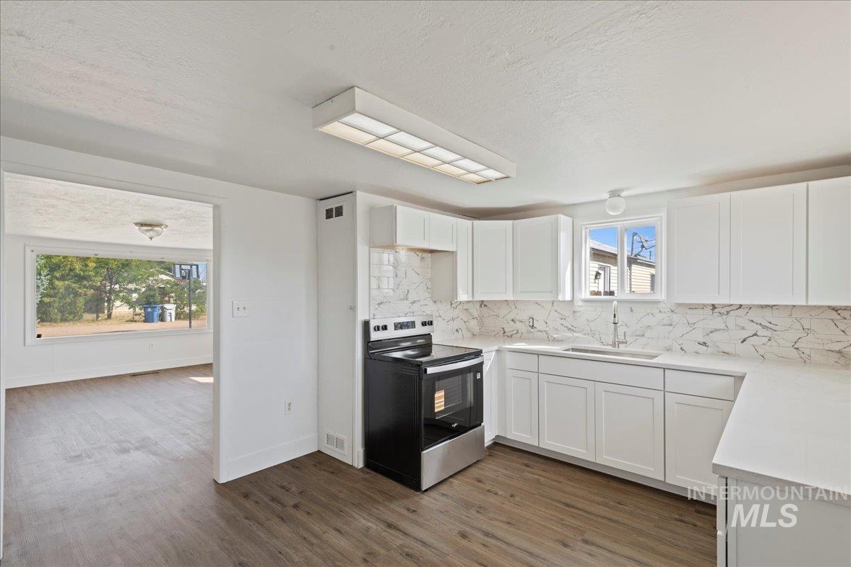 Kitchen with electric stove, white cabinets, backsplash, dark wood finished floors, and a textured ceiling