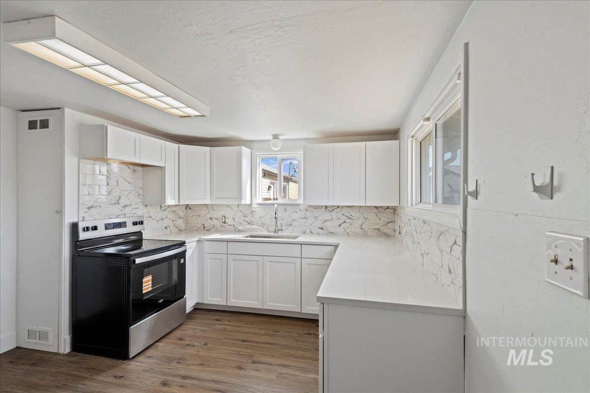 Kitchen with stainless steel electric range oven, white cabinetry, dark wood-type flooring, tasteful backsplash, and light stone countertops