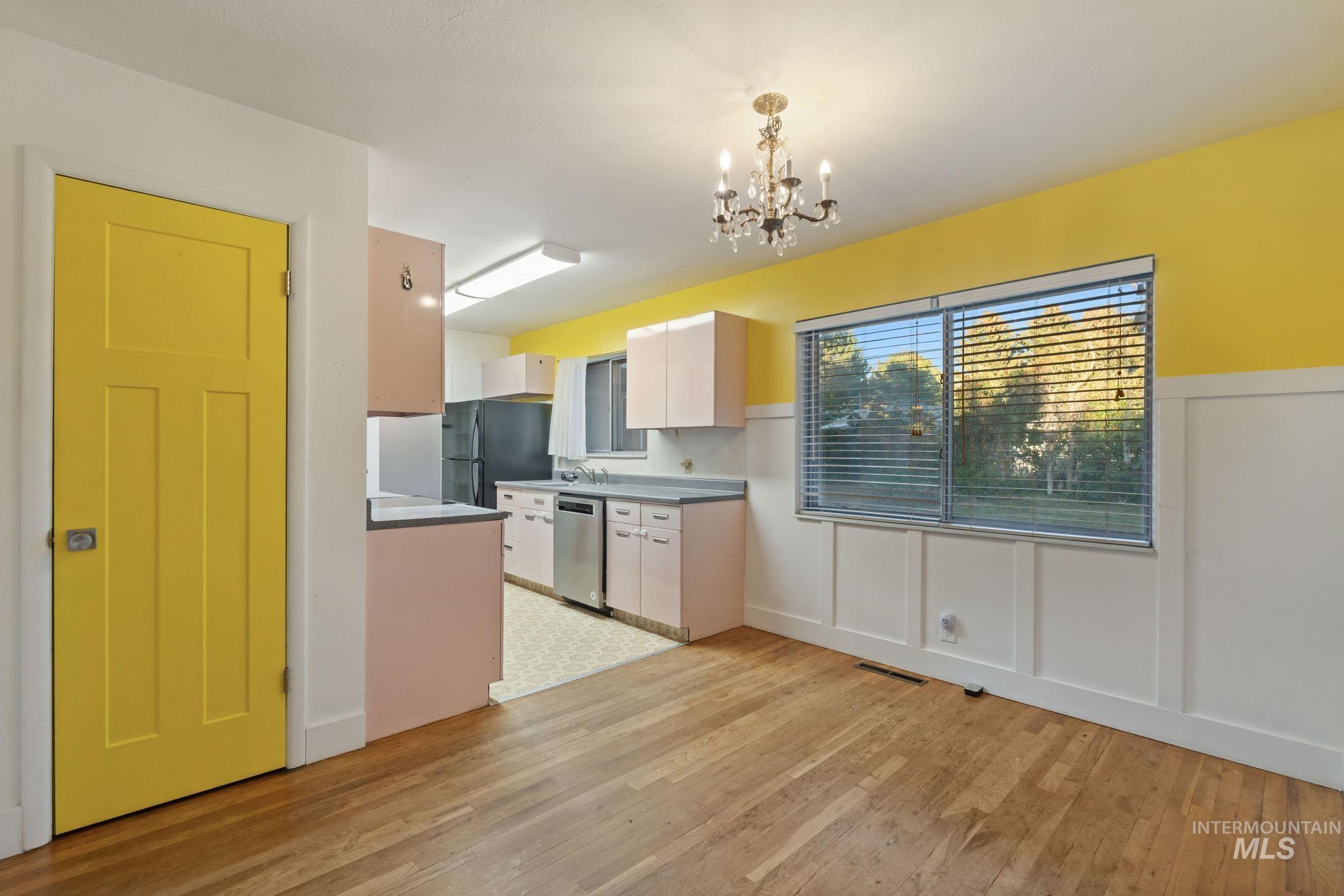Kitchen with light wood-style floors, white cabinets, decorative light fixtures, stainless steel dishwasher, and a chandelier