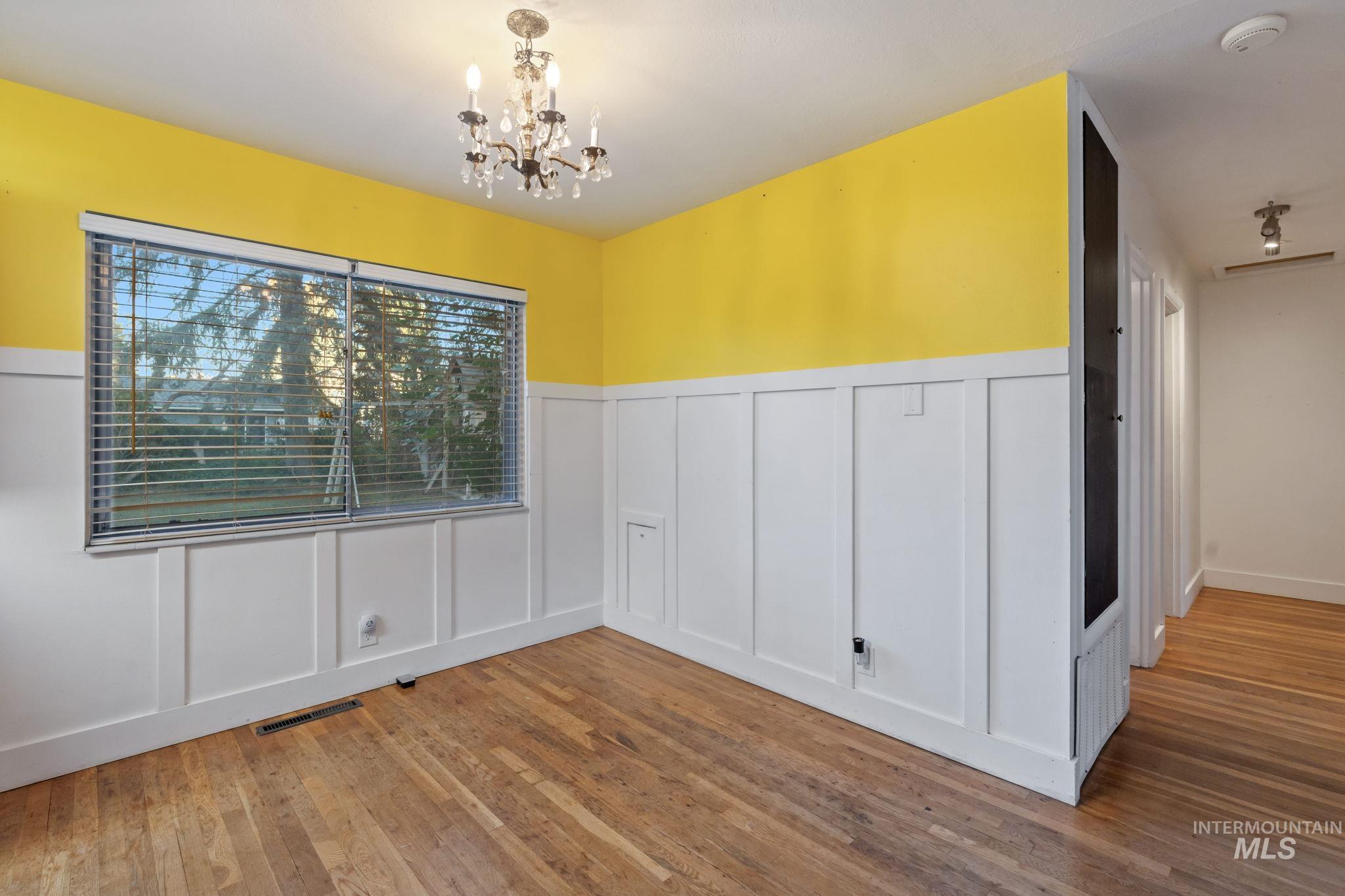 Unfurnished dining area featuring a decorative wall, wainscoting, a chandelier, and hardwood / wood-style flooring