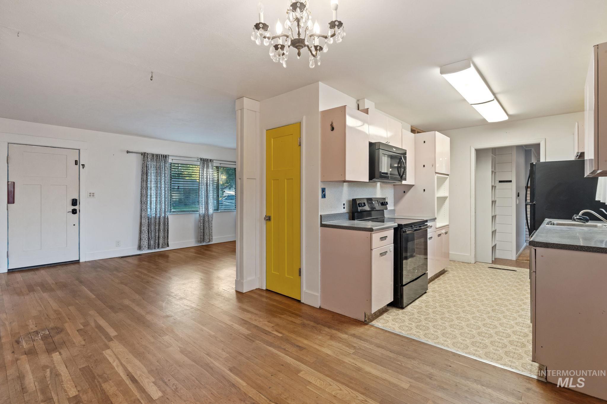 Kitchen with black appliances, a chandelier, light wood finished floors, white cabinetry, and dark countertops